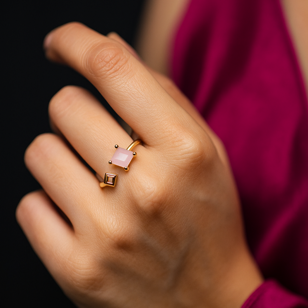 Hand wearing a pink gemstone ring with gold band against a dark background