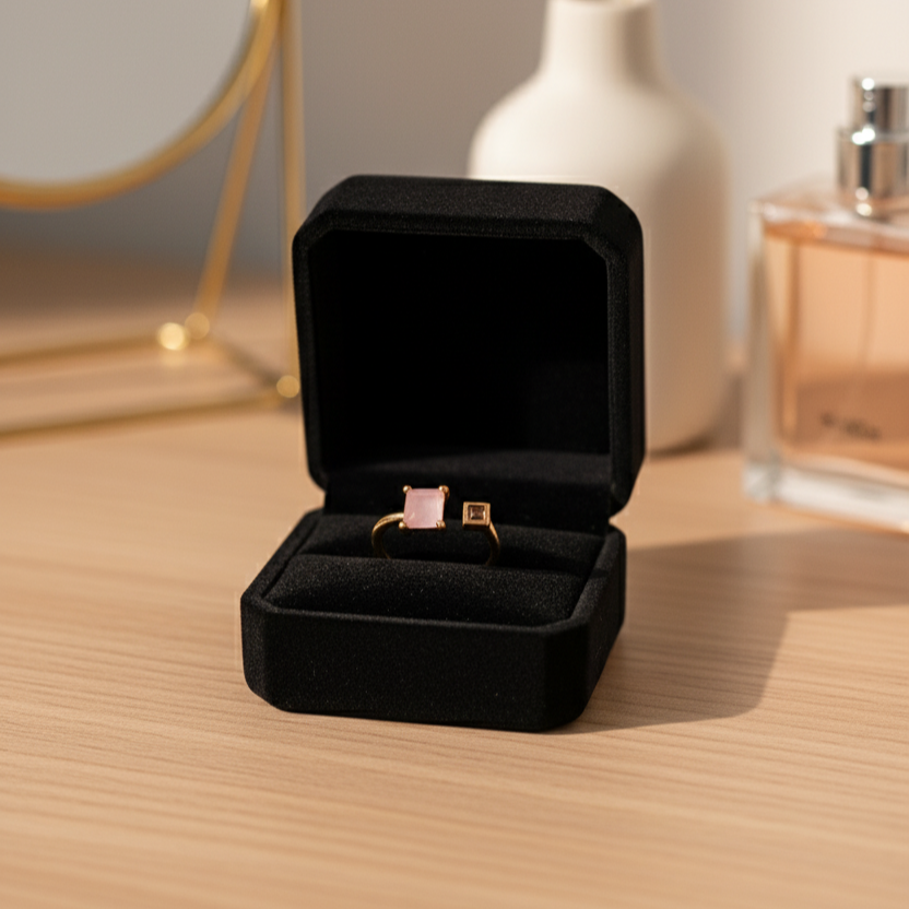 Black jewelry box with a ring on a wooden surface, with a mirror and bottle in the background.