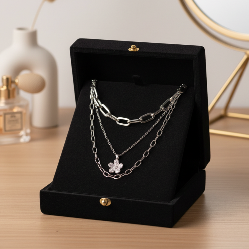 Silver chain necklace on a black jewelry display box with a perfume bottle and decorative items in the background.