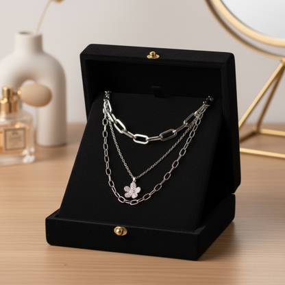 Silver chain necklace on a black jewelry display box with a perfume bottle and decorative items in the background.