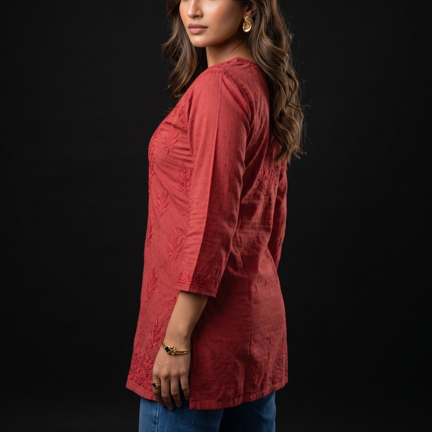 Woman wearing a red textured top and blue jeans against a black background
