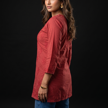 Woman wearing a red textured top and blue jeans against a black background